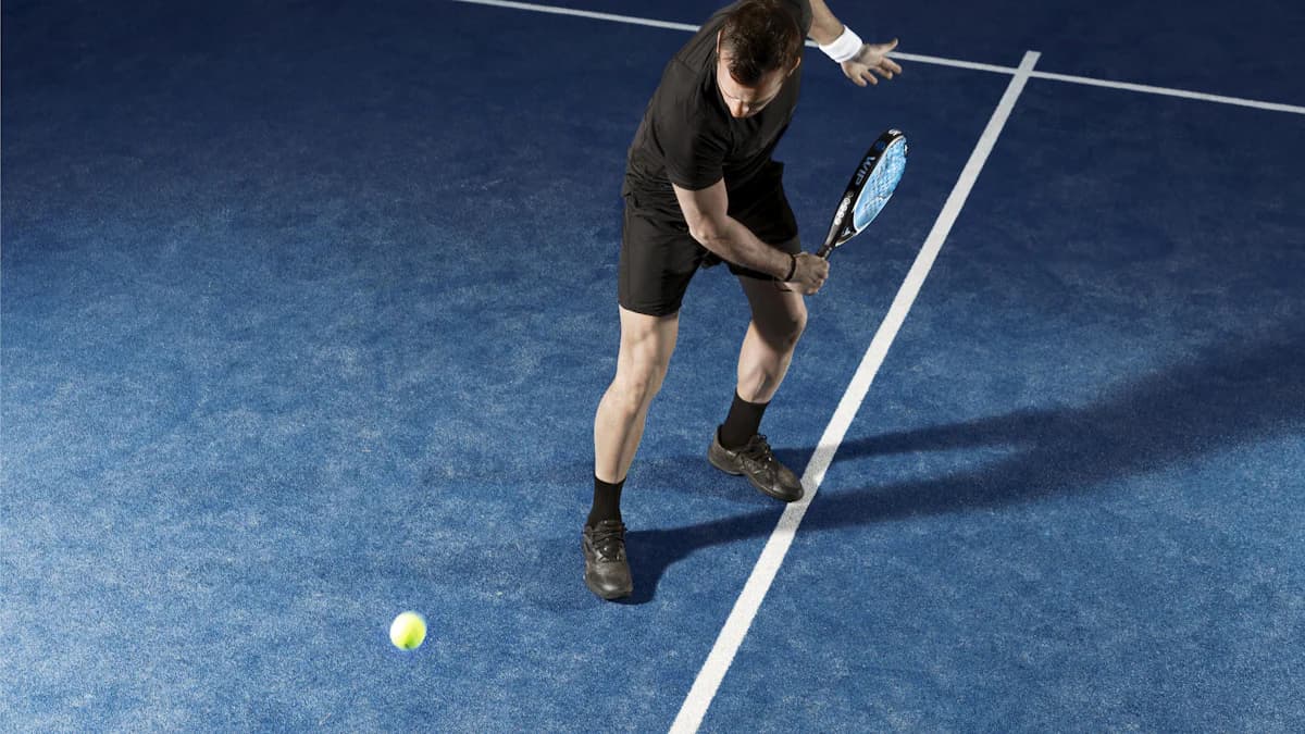 Padelspiller i aktion på en blå padelbane med bold i luften